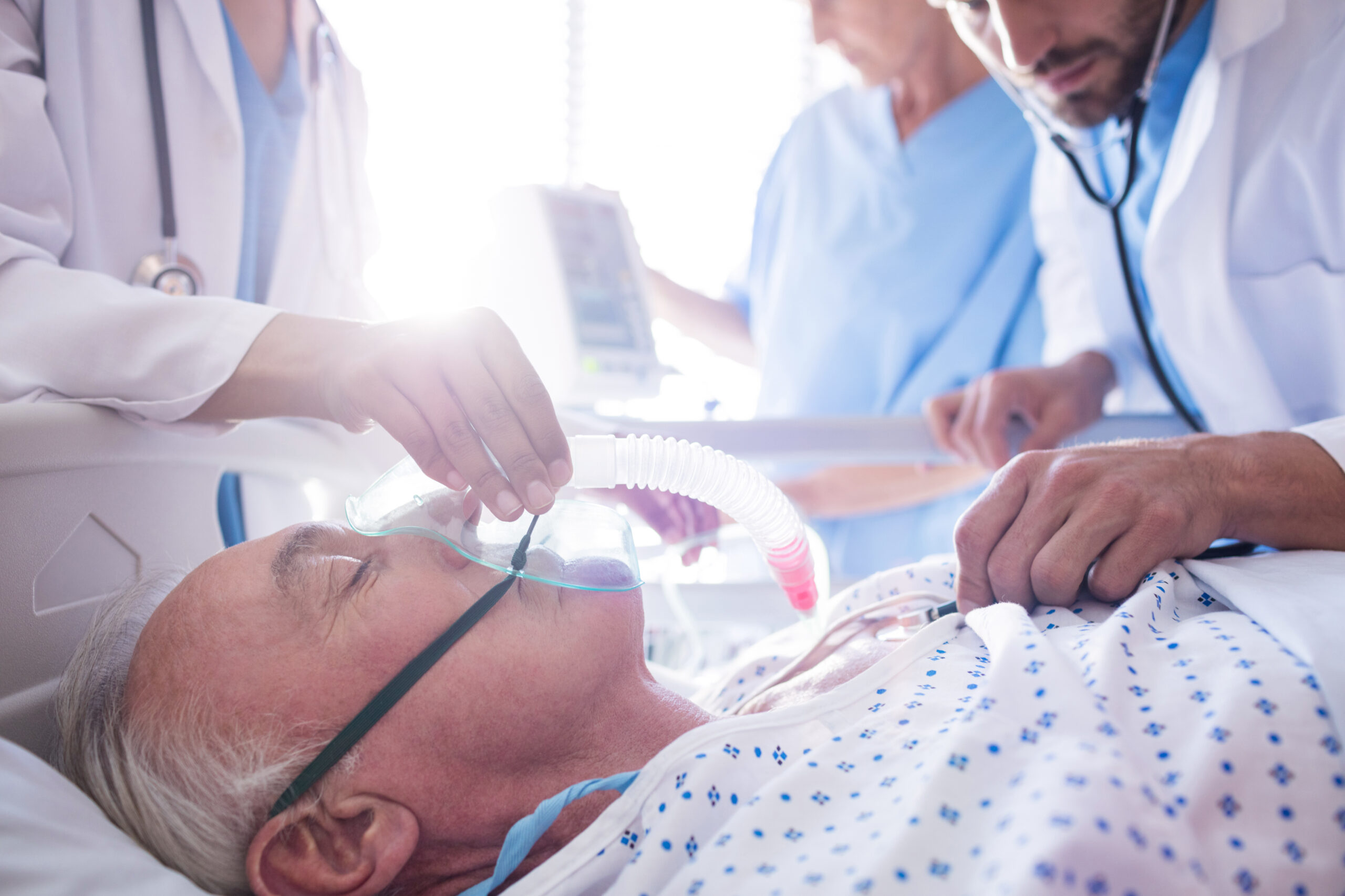 Team of doctors putting oxygen mask on a male senior patient face in the hospital